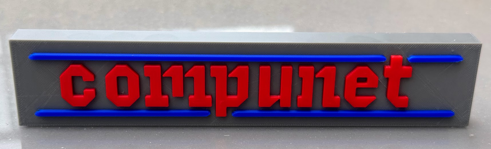 The printed Compunet plaque head-on: red lettering between two blue rules on a grey slab